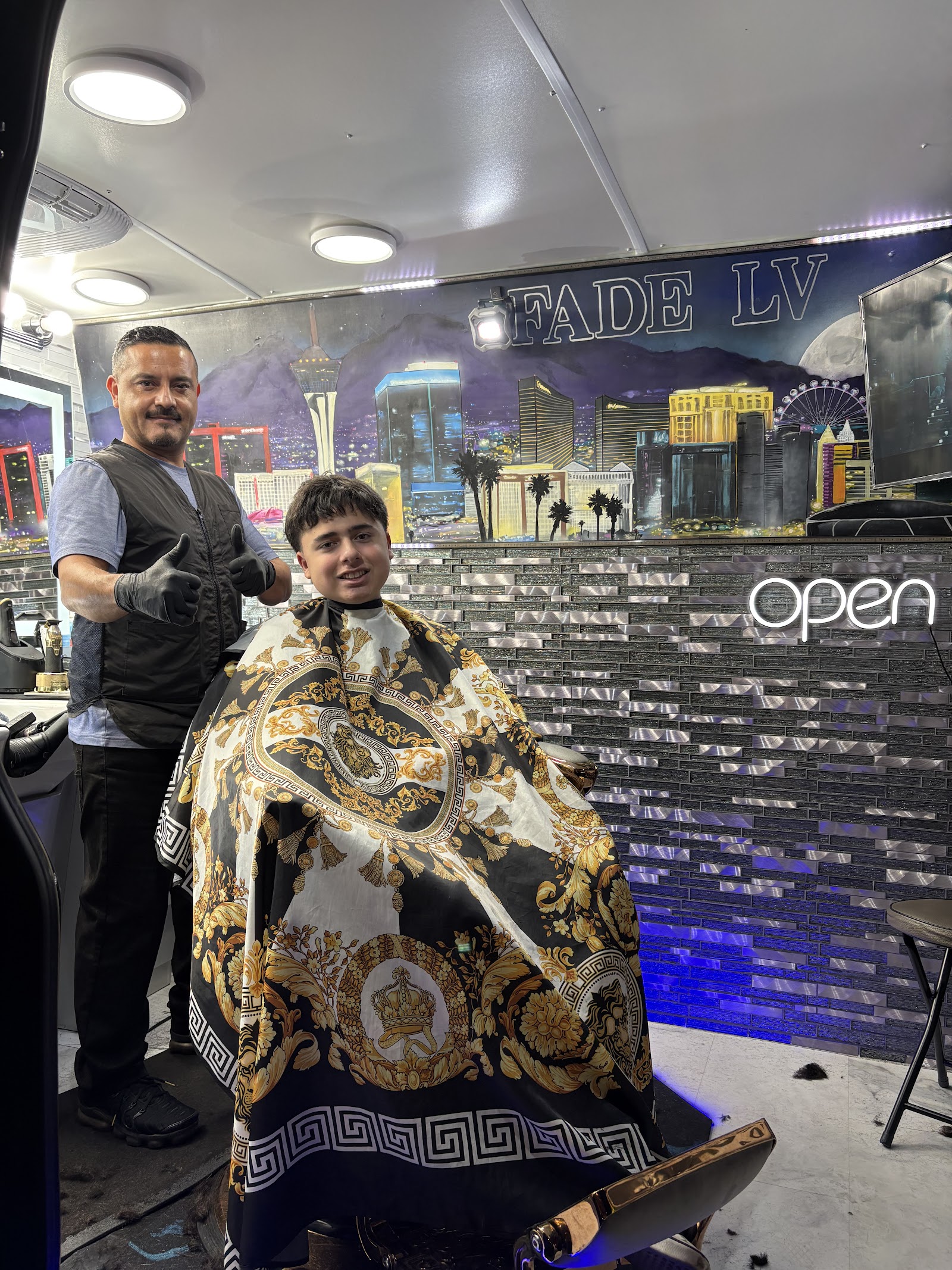 Barber giving a thumbs up next to a smiling young client caped up in the barber chair
